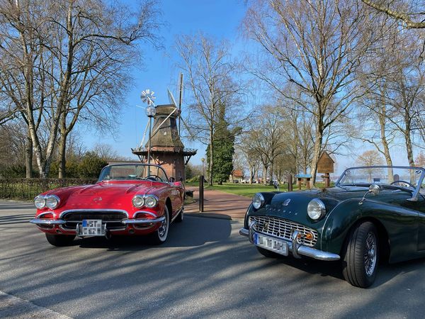 Roter Chevrolet Corvette und grüner Triumph Cabrio vor der Windmühle im Kurpark mit kahlen Bäumen.