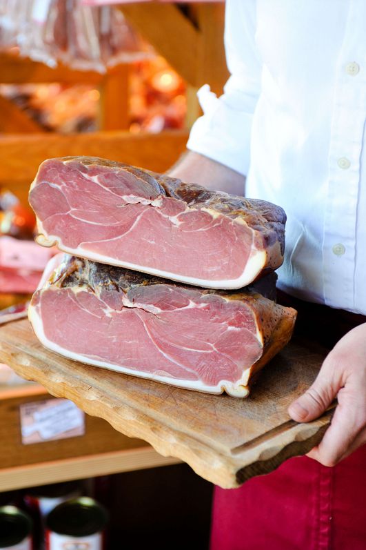 Zwei aufeinander aufgeschnittene Schinken auf einem Brett, getragen von einem Kellner.