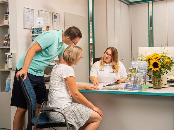 Eine Touristik-Mitarbeiterin zeigt in der Tourist-Information einem Pärchen einen Flyer.