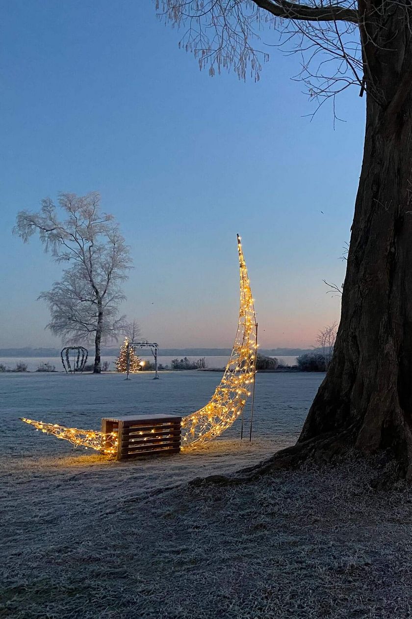 Winterliche Szene in der Winter-Wunder-Welt Bad Zwischenahn mit beleuchteten Mondsicheln im Kurpark, funkelnden Lichtern und frostiger Atmosphäre bei Sonnenaufgang.