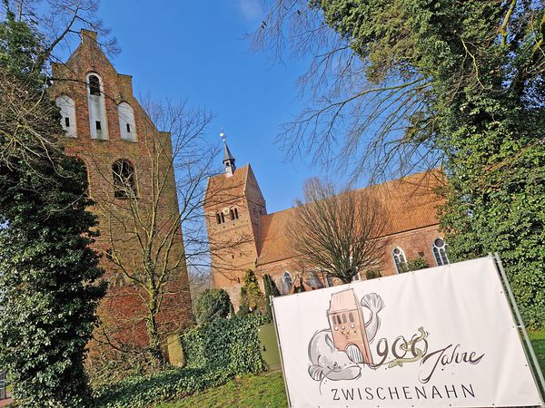 Bauzaun mit dem Logo 900 Jahre Zwischenahn vor der St. Johannes Kirche.