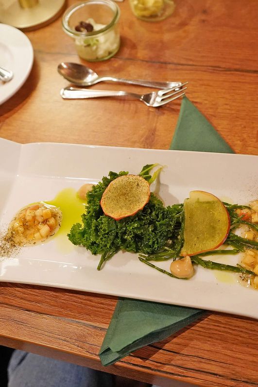 Ansprechend angerichteter Teller mit Grünkohl, Apfel und Soße auf einem Holztisch mit Besteck.