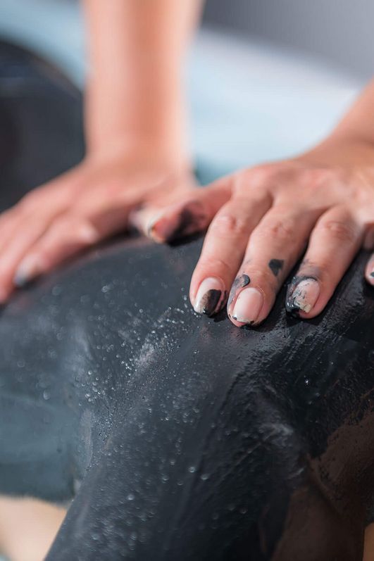 Moorschlammmassage mit den Händen am Rücken einer Frau.