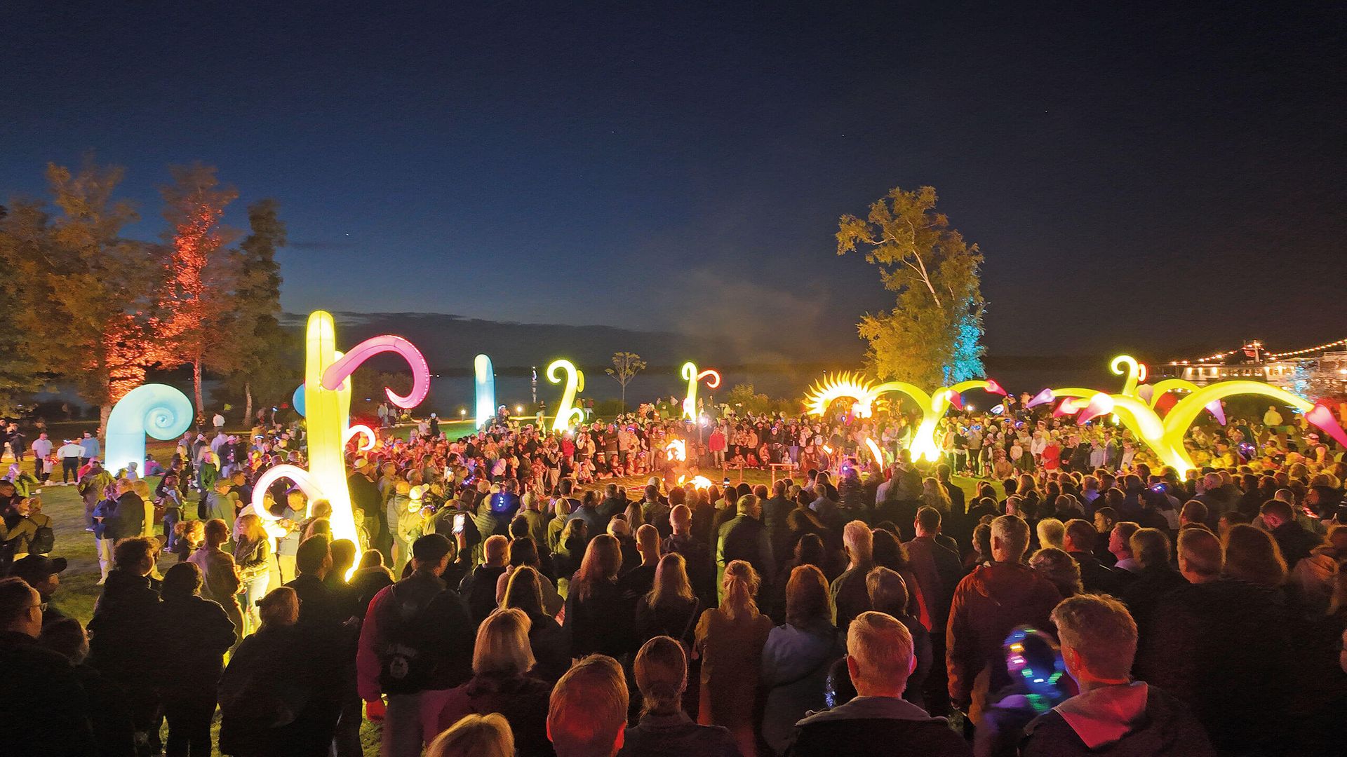 Große Menschenmenge bei Nacht im Kurpark bei einer Feuershow, leuchtende, bunte, Lichtinstallationen im Hintergrund.