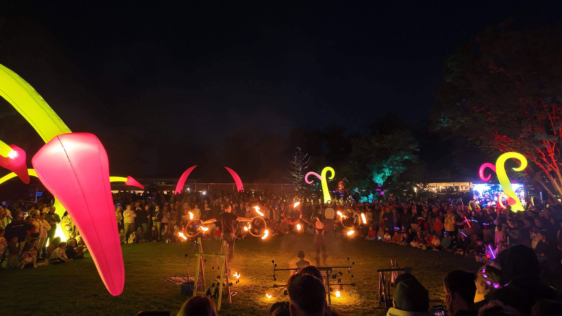 Feuershow mit mehreren Künstlern vor großem Publikum im Kurpark bei Nacht mit bunten Lichtinstallationen.