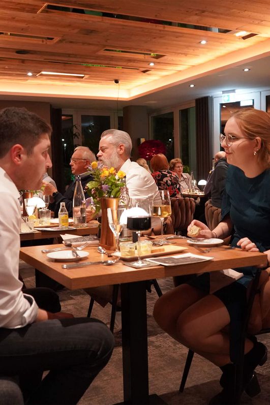 Paar sitzt bei gedämpftem Licht an einem gedeckten Holztisch in einem Restaurant, umgeben von weiteren Gästen.
