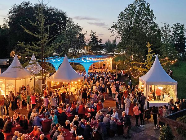 Besucher genießen bei sommerlichem Wetter das Weinfest im Kurpark am Zwischenahner Meer mit Weinständen und Live-Musik auf der Freilichtbühne. .