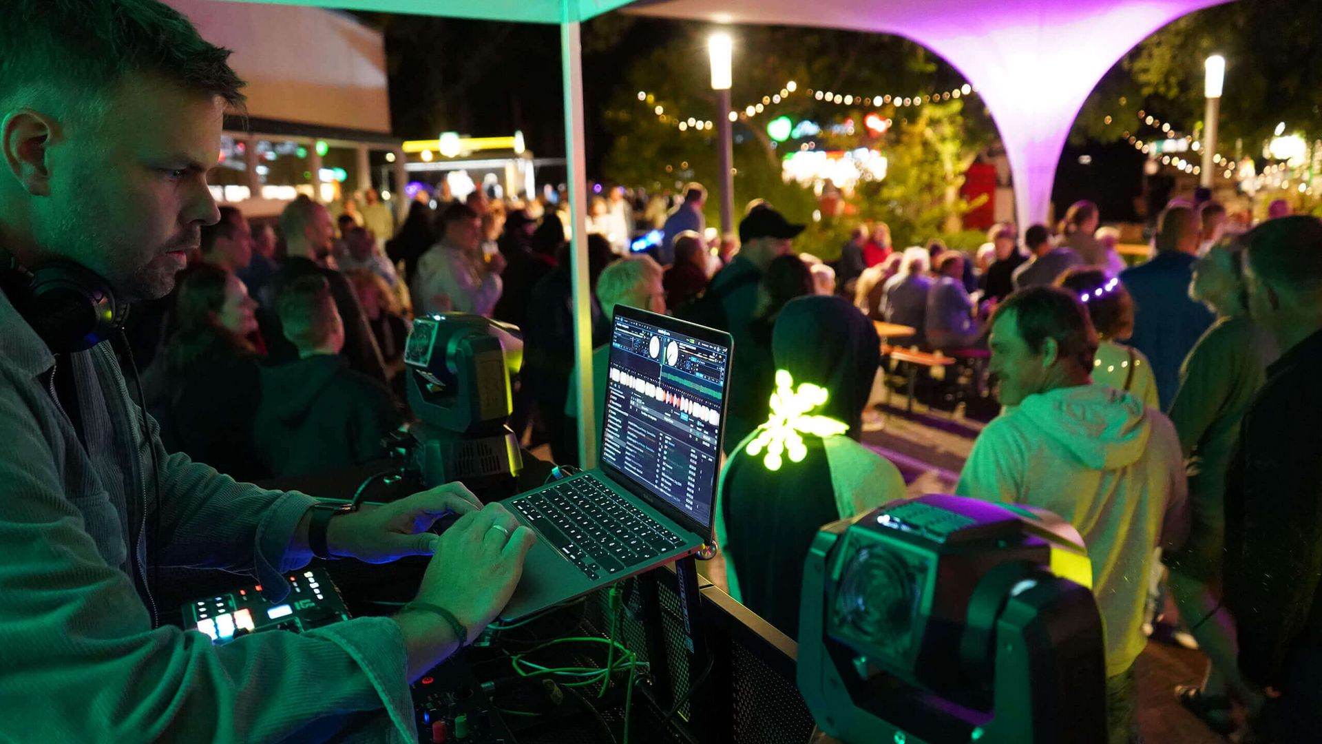 DJ Thi Rex bedient Laptop und Mischpult unter einem Zeltdach vor einer tanzenden Menschenmenge bei Nacht auf der Terrasse der Wandelhalle.