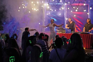Menschen tanzen auf der Open-Air-Silent-Party mit Kopfhörern vor einem DJ-Pult unter Lichterketten auf der Freilichtbühne.