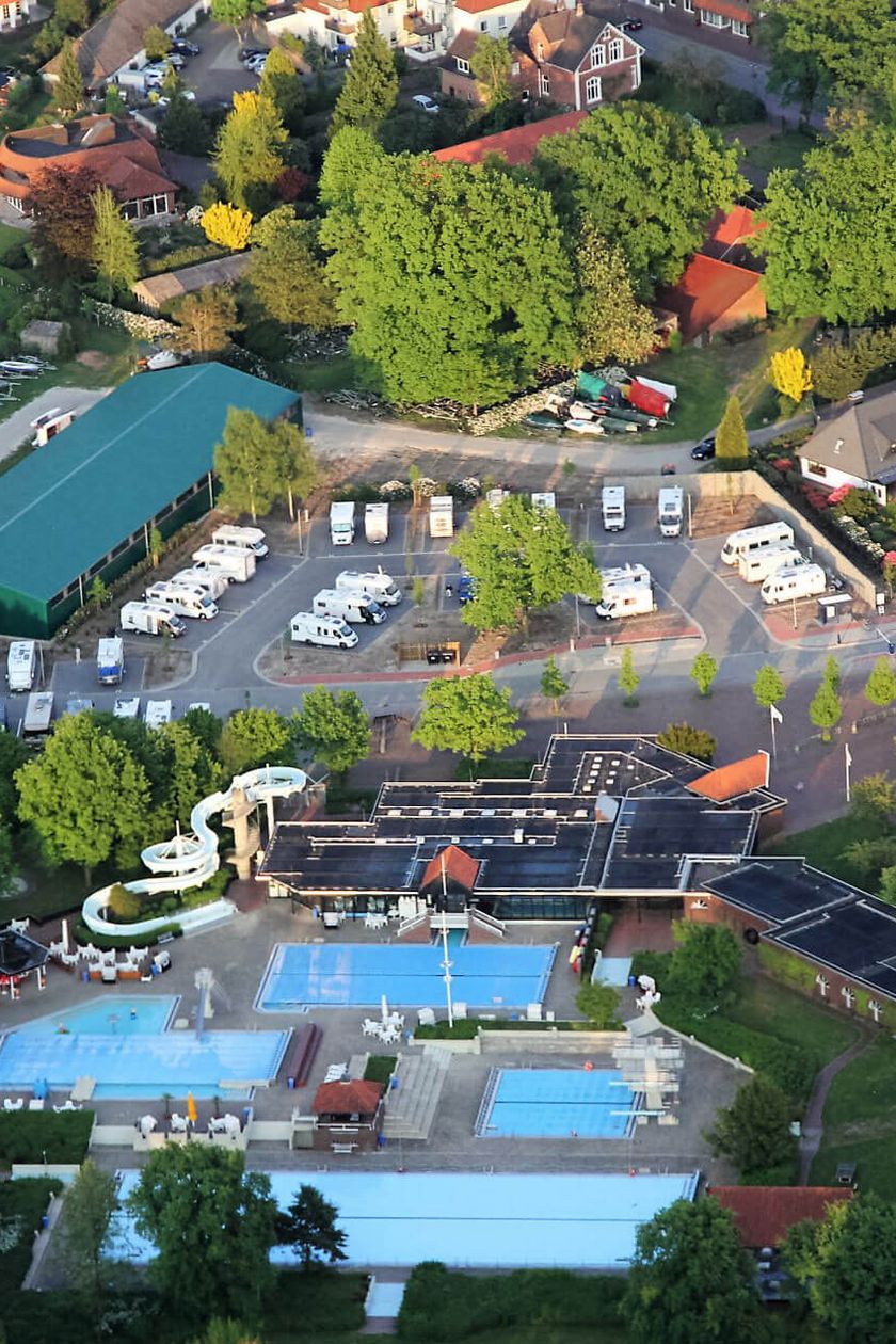 Luftaufnahme des Wohnmobilstellplatzes am Badepark mit geparkten Fahrzeugen und den Badepark im Vordergrund.