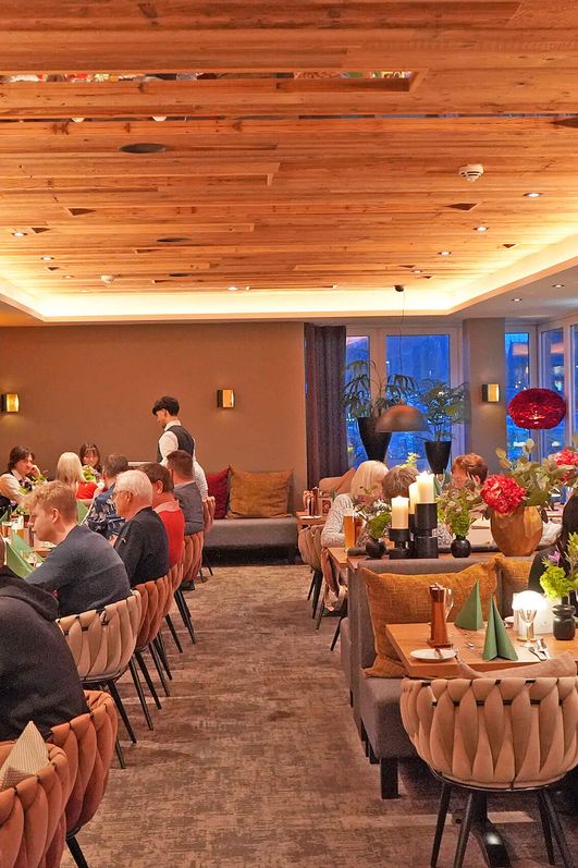 Innenraum im Restaurant Delikat mit mehreren Gästen an gedeckten Tischen und warmem Holzdekor an der Decke.