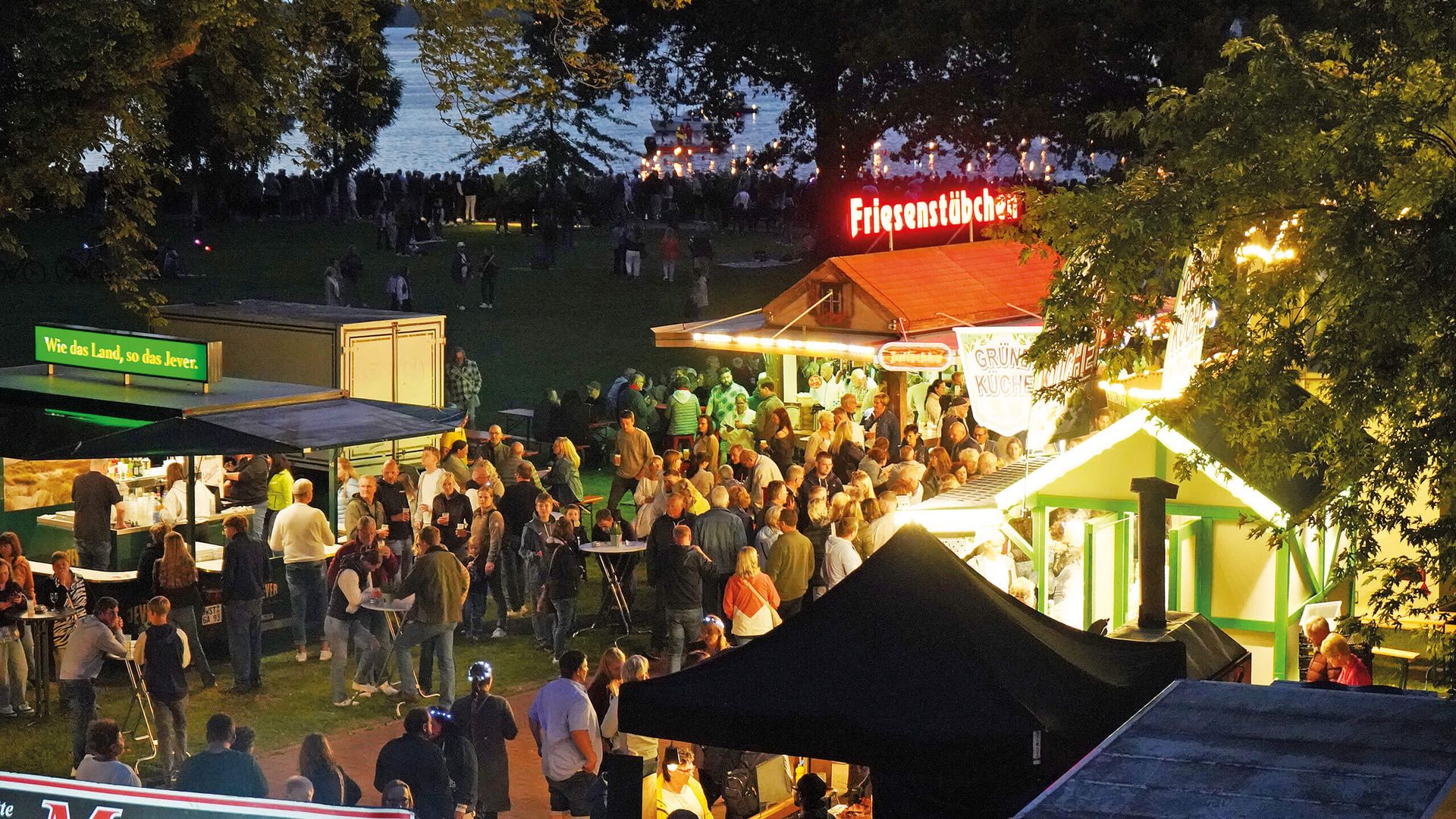 Menschenmenge bei abendlicher Lichternacht im Kurpark mit beleuchteten Ständen und Bäumen im Hintergrund.