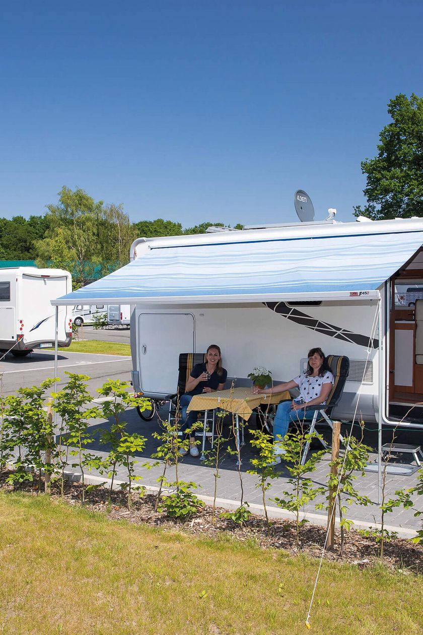 Zwei Frauen sitzen unter der Überdachung eines Wohnmobils bei Sonnenschein.