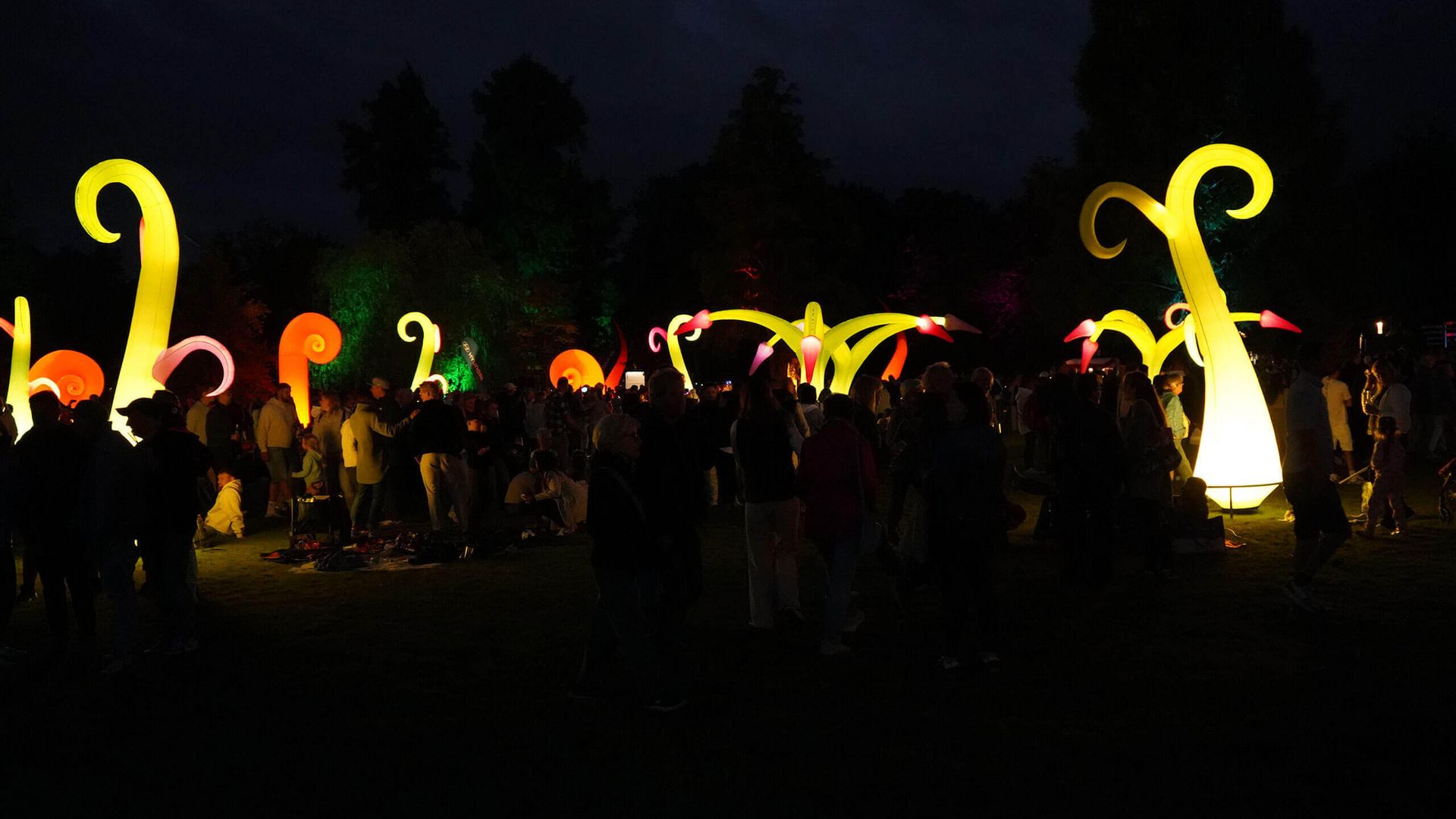 Leuchtende Installationen in Gelb und Orange auf der kurparkwiese bei Nacht mit vielen Menschen.